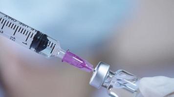 Nahaufnahme der Krankenschwester mit Spritze saugt einen Coronavirus-Impfstoff aus der Flasche, mit ihren Händen tragen sie Gummihandschuhe und Gesichtsmaske, moderne medizinische Gesundheitsschutzkonzepte, anästhetische Injektionsspritze, video