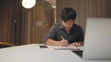 fleißiger asiatischer geschäftsmann im schwarzen hemd, der auf klemmbrettdokument mit laptop schreibtisch überprüft, datenanalysemanagement, junger unternehmer denkt planer, arbeitet an checkliste, geschäftstechnik video