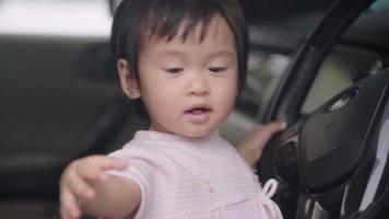 Lernfähigkeiten für die Entwicklung von Kindern, Zeit damit verbringen, Spaß im Fahrzeug zu haben und mit dem Lenkrad zu spielen, Babysitten auf dem Autofahrersitz, glückliches Mädchen, das sich selbst freut, wenn es so tut, als würde es fahren video
