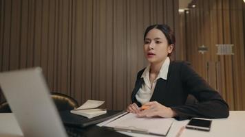 jonge aziatische werkende vrouw probeert te denken aan de nieuwe creatieve ideeën voor zakelijke zakelijke bijeenkomsten, concentreert zich terwijl ze alleen aan het bureau zit, serieuze dame werkt aan het oplossen van problemen voor clents video