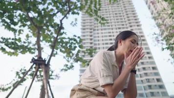 Asian girl feel disappointing and sad sit down in the middle of high rise buildings condominium apartments, showing frustration and pressured emotion, outdoor under the trees shot. Human emotions video