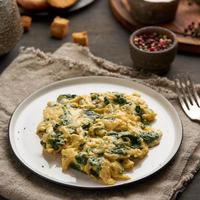 Scrambled eggs with spinach, cup of tea on dark brown background photo