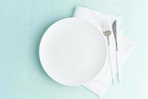 plato blanco vacío limpio, tenedor y cuchillo sobre una mesa de piedra turquesa azul verde, espacio de copia, maqueta foto