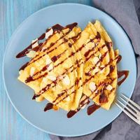 Two pancakes with chocolate syrup, almond flakes on plate, honey flows from spoon, top view, macro photo