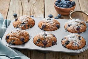 Blueberry muffin in tray, side view. Cupcakes with berries in baking dish on old linen napkin, rustic wooden table, breakfast with cake photo