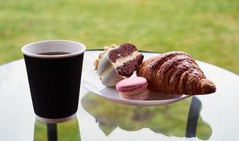 desayuno con croissant y postre, café o té en taza de plástico, en el pueblo, al aire libre, naturaleza. foto
