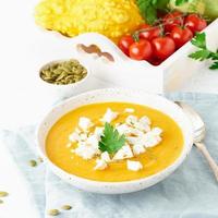 Pumpkin cream soup with feta cheese, autumn homemade food, white background, closeup