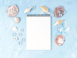 Mock up with frame of seashell, notepad on blue stone backdrop, copy space. Summer concept photo