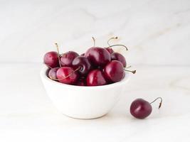 red dark sweet cherries in white bowl on stone white table, side view. photo
