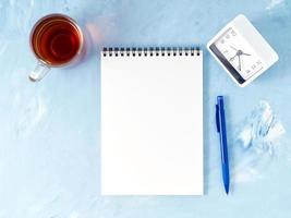 Top view of modern bright blue office desktop with notepad, clock, flower succulent. Mock up, empty space photo