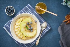 Oatmeal with bananas, blueberries, jam, honey, blue napkin on blue stone background photo