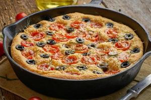 Focaccia, pizza in skillet. Close up italian flat bread with tomatoes, olives and rosemary photo