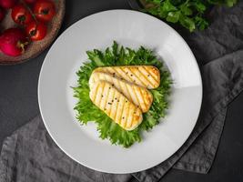 Grilled Halloumi, fried cheese with lettuce salad. Balanced diet, white plate on dark background, top view photo