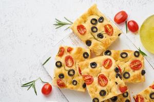 Sliced pieces of focaccia with tomatoes, olives and rosemary.