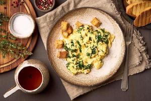 Pan-fried scrambled eggs and spinach, cup of tea on dark brown background photo