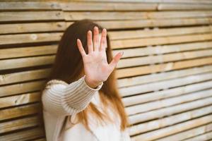 Woman with long hair reaches forward, shielding her face from camera. Concept of privacy, personal space, prohibition of photography. A woman sits on wooden bench. Stop, taking pictures is forbidden photo