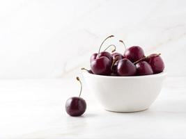 cerezas dulces rojas oscuras en un tazón blanco sobre una mesa blanca de piedra, vista lateral, espacio para copiar