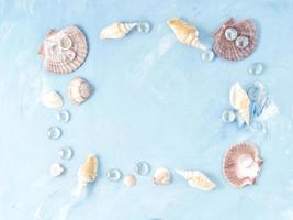 maqueta con marco de concha marina sobre fondo de piedra azul, concha de vieira, espacio de copia. concepto de verano foto