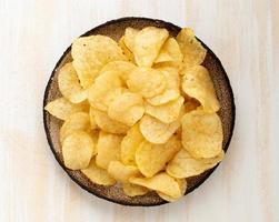brown yellow chips from natural potato in brown ceramic plate on white wooden background