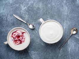 Greek yogurt with jam in white bowl on grey blue concrete stone table, top view, copy space photo