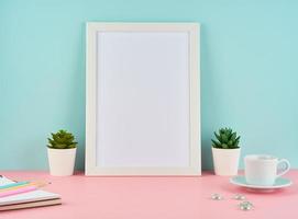 Mockup with blank white frame, plant cactus, cup of coffee or tea on pink table photo