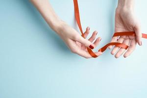 woman hands holding red ribbon, design concept on aquamarine background, copy space photo