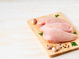 raw chicken breast fillet with spices on wooden board on white wooden table photo