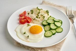 Healthy breakfast - fried egg with cherry tomatoes and cucumber on light white background, fodmap dash diet, gluten free, side view closeup photo