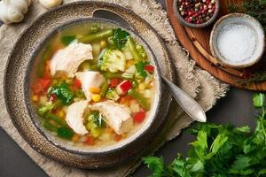 Homemade chicken soup with vegetables, broccoli on a dark brown background, top view photo