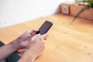 primer plano de las manos del hombre sosteniendo el teléfono móvil con espacio de copia en blanco. hipster adolescente mirando en el teléfono inteligente en el café foto