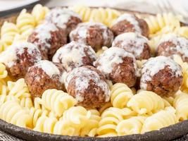 Swedish meatballs with sauce and fusilli paste on white wooden table, close up, side view photo