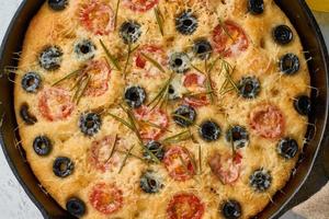 Focaccia, pizza in skillet, italian flat bread with tomatoes, olives and rosemary. Wooden table photo