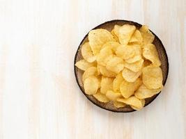 chips amarillos marrones de patata natural en placa de cerámica marrón sobre fondo de madera blanca foto