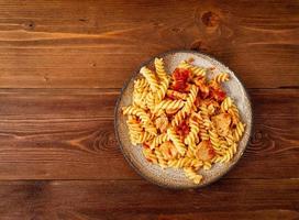 fusilli pasta with tomato sauce, chicken fillet on dark brown wooden background, cope space, top view photo