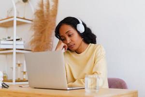 estudiante afroamericana aburrida y cansada viendo clases a distancia en línea en una laptop foto