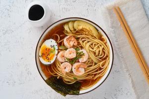 Asian soup with noodles, ramen with shrimps, miso paste, soy sauce. White stone table