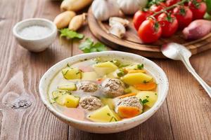 meatballs soup in white plate on old wooden rustic brown table, side view photo