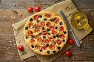 Focaccia, pizza, italian flat bread with tomatoes, olives and rosemary on wooden rustic table photo