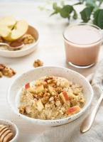 Oatmeal with apple, walnuts and cup of cocoa on white wooden light background photo