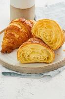 Two delicious croissants on plate and hot drink in mug. Croissant sectional view, photo