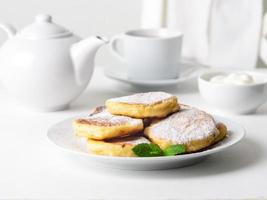 Cheesecake, curd fritters. Cottage cheese pancakes with powdered sugar. Sweet fried cheese pancakes on white plate on white background. Home tea party photo