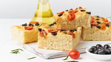 Focaccia with tomatoes, olives and rosemary, side view. Traditional Italian flat bread photo