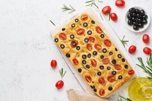 Focaccia with tomatoes, olives and rosemary, copy space, top view. Whole Italian flat bread,