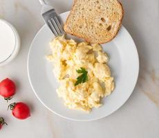 white plate with pan-fried scrambled eggs on white light background with tomatoes. Omelette, top view photo