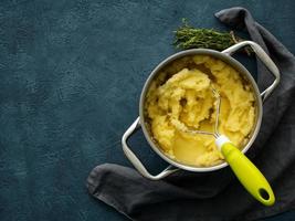 Mashed potatoes in bowl on dark stone blue table, rosemary, napkin, top view photo