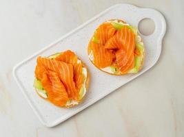 Two open sandwiches with salmon, cream cheese, cucumber slices on white marble table