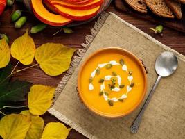 Autumn food. Pumpkin puree soup, leaves, dark brown old wooden table, top view.