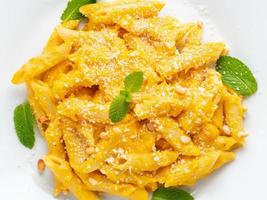 Pumpkin pasta penne with parmesan on white plate, top view, close-up