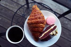 Breakfast with croissant and dessert, coffee or tea in plastic mug, in the village, outdoors, nature. photo