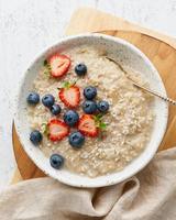 Oatmeal porridge rustic with berries, dash diet, on white wooden background top view
